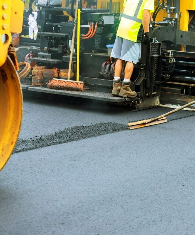 Road roller at a road construction site, paver laying fresh asphalt pavement during road